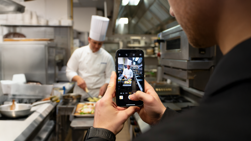 Mann filmt mit seinem Smartphone den Koch in einer Küche. Mann filmt mit seinem Smartphone den Koch in einer Küche.